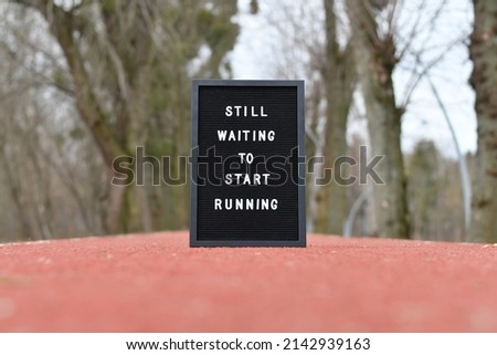 'Still waiting to start running' letters on black letterboard put on running track with artificial coating outdoors. 