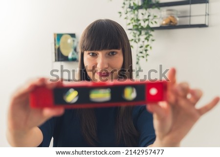 Caucasian brown-haired woman looking at camera while holding a sprit level. Indoor shot. High quality photo