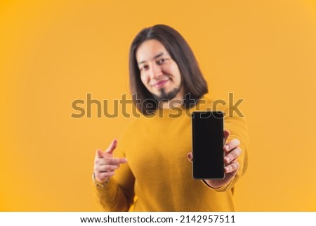 Cheerful bearded caucasian man showing his smartphone with blank screen. Technology concept. Studio shot over orange yellow background. High quality photo