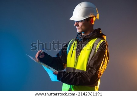 Builder draws blueprints. Construction company manager. Man holding construction blueprint. Room drawings in hands of engineer. Architect in yellow vest. Builder in protective helmet. Builder on dark Royalty-Free Stock Photo #2142961191