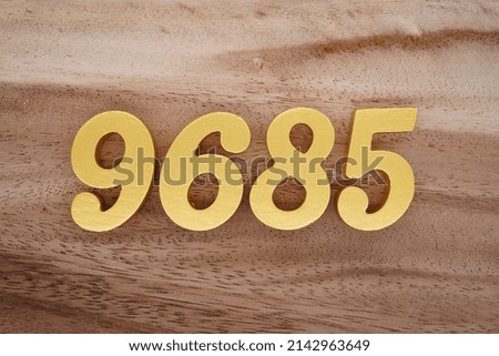 Wooden  numerals 9685 painted in gold on a dark brown and white patterned plank background.