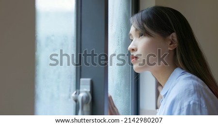 close up asian lonely woman is looking the rain falling through a window at home Royalty-Free Stock Photo #2142980207