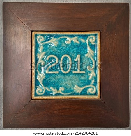 Typical room number plate in ceramics with wooden frame.