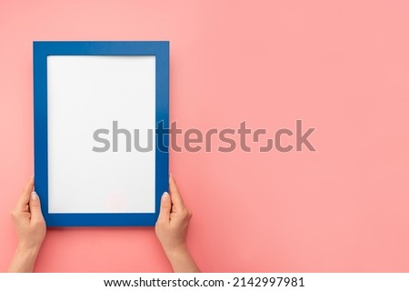 Woman hold blank diploma frame on pink wall background. Female hands hold empty mockup frame. Cropped hand of woman holding picture frame against pink wall. copy space
