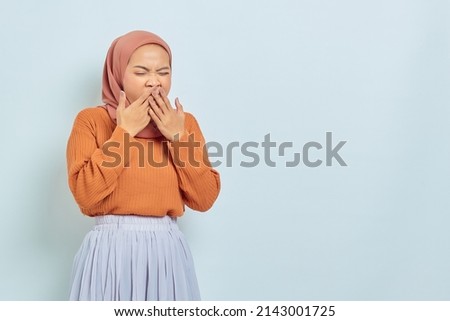 Beautiful Asian woman in brown sweater and hijab covering mouth and feeling sleepy isolated on white background.