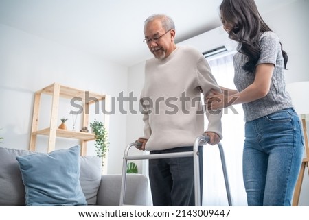 Asian young daughter support senior older man walk with walker at home. Beautiful girl help and take care of elderly mature grandpa patient doing physical therapy for health in living room in house. Royalty-Free Stock Photo #2143009447