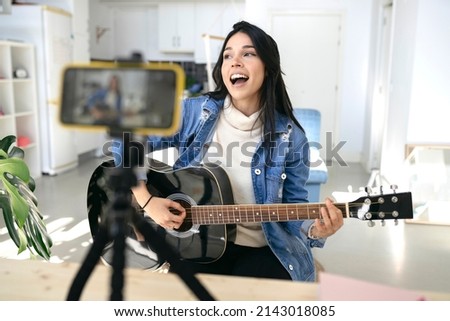 influential young woman playing guitar during podcast or live video broadcast for the audience from the mobile phone at home - concept art, hobby and video blog Royalty-Free Stock Photo #2143018085