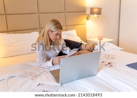 Businesswoman in suit talking on smartphone and looking at notebook in hotel room. Business Woman working from a hotel room. Beautiful young woman talking on mobile smart phone.