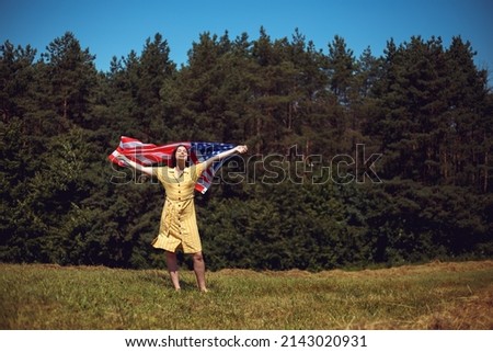 Happy 4th of July! Independence Day celebrating. Patriotic woman hold wrapped in american national flag waving on wind and walking on the field. Stars and stripes. Freedom concept.