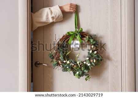 Woman hanging Easter wreath on wooden door, closeup Royalty-Free Stock Photo #2143029719