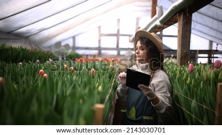 Florist woman in hat takes inventory in a flower shop, a female uses a screen tablet to count the number of flowers. Pretty woman working in flower shop selling plants online