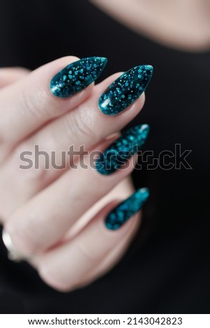 Woman hand with long nails and teal blue green manicure with bottles of nail polish