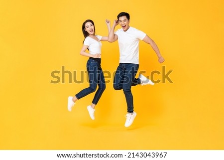 Happy energetic smiling Asian couple wearing casual clothes jumping in studio isolated yellow color background