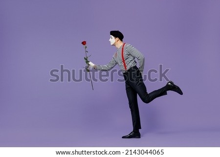 Full size body length side view profile young mime man with white face mask wears striped shirt beret run go give present rose flower isolated on plain pastel light violet background studio portrait