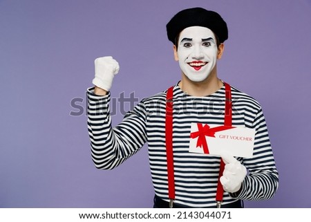 Fun young mime man with white face mask wears striped shirt beret hold gift certificate coupon voucher card for store do winner gesture isolated on plain pastel light violet background studio portrait