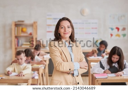 Waist up portrait of smiling female teacher looking at camera while posing confidently standing with arms crossed in school classroom, copy space Royalty-Free Stock Photo #2143046689