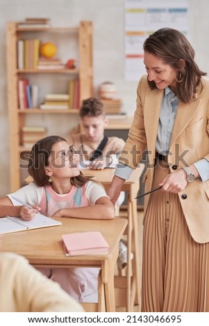 Vertical portrait of young female teacher smiling while helping children during class in school, copy space Royalty-Free Stock Photo #2143046695
