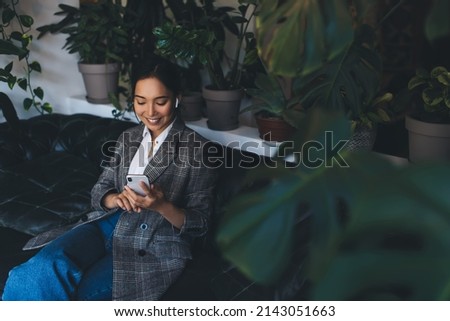 Cheerful female blogger enjoying time for mobile networking browsing website with record podcast,happy Asian woman in bluetooth earbuds listening positive music and received audio message on cellphone