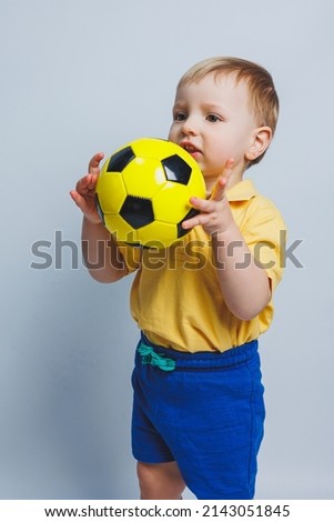 Little cute kid baby boy 3-4 years old, football fan in red t-shirt holding in hand soccer ball isolated on yellow background. Kids sport family leisure lifestyle concept. Copy space advertisement