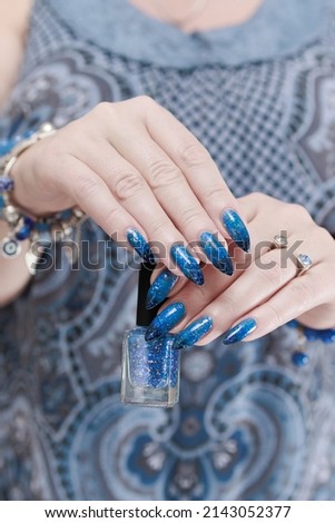Female hand with long nails and blue-black thermo french nail polish
