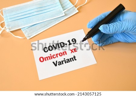 Covid-19 new Omicron XE. Hand of the doctor in blue glove with marker and writing "Covid-19 Omicron XE" on white sheet. Medical face mask. Concept for the new Covid 19 Omicron variant Royalty-Free Stock Photo #2143057125