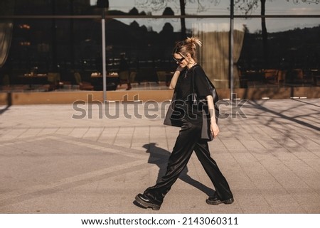 Details of everyday elegant black and grey look. Model wearing casual outfit. Grey jacket, black bag, t-shirt, pants and boots in trendy minimalistic style. Street fashion for spring or fall season. Royalty-Free Stock Photo #2143060311