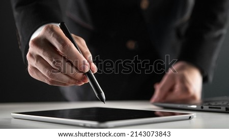 Close up of businessman using electronic pencil or stylus pen signing contract on digital tablet with laptop computer on office table