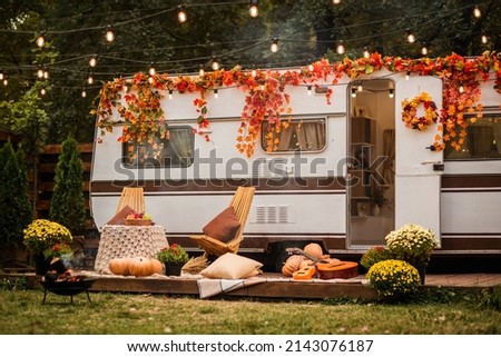 Wooden table and chairs near the trailer. camping autumn.  Trailer on the background of the forest. Flowers in pots.Guitars