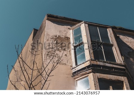 Old dilapidated Victorian end of terrace property in a town centre featuring a bay window with rotten frame and peeling plaster against a blue sky Royalty-Free Stock Photo #2143076957