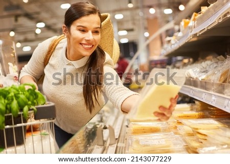 Smiling young woman at the refrigerated section in the supermarket buying cheese and reading shelf life information Royalty-Free Stock Photo #2143077229