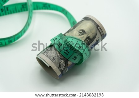 The tape measure tightly bound the $100 bill. Currency devaluation, economic crisis, rising prices, inflation.collapse, stagnation economy. Royalty-Free Stock Photo #2143082193