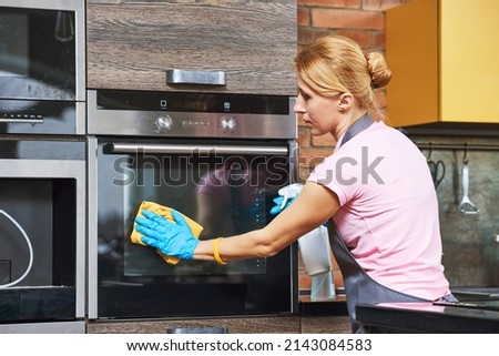 Cleaning service. woman cleaning and wiping kitchen oven with cloth Royalty-Free Stock Photo #2143084583