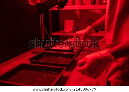 Unrecognizable young man with protective gloves on hands working in darkroom poring photo developing liquid into plastic containers