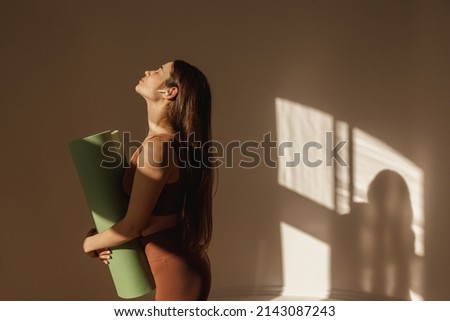 Side view of fit caucasian young girl with mat recovering after indoor workout. Athletic lady with long dark hair in top and leggings. Wellness concept. Royalty-Free Stock Photo #2143087243
