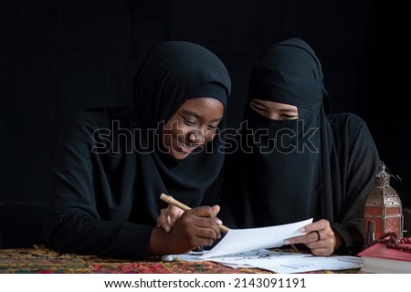 Muslim women wearing black hijab learn to writing Arabic calligraphy with ink together, black background