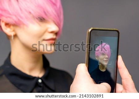 Man hairdresser's hands taking picture on smartphone of her client short pink hairstyle