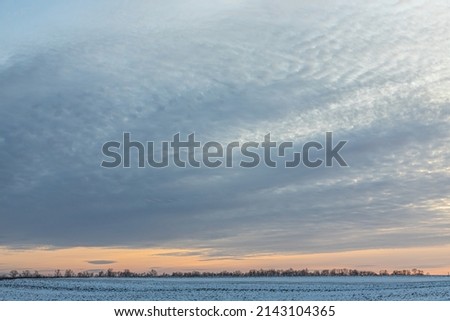 Natural sunset sunrise over field or meadow. The color of the sky over the winter snowy ground. Landscape under a picturesque sky at sunset. Dawn of the sun. Skyline, Horizon.
