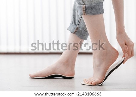 Woman fitting orthopedic insole indoors, close up. Girl holding an insole next to foot at home. Orthopedic insoles. Foot care banner. Flat Feet Correction. Treatment and prevention of foot diseases. Royalty-Free Stock Photo #2143106663