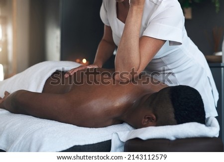 Working out the tension. Shot of a young man getting a back massage at a spa. Royalty-Free Stock Photo #2143112579