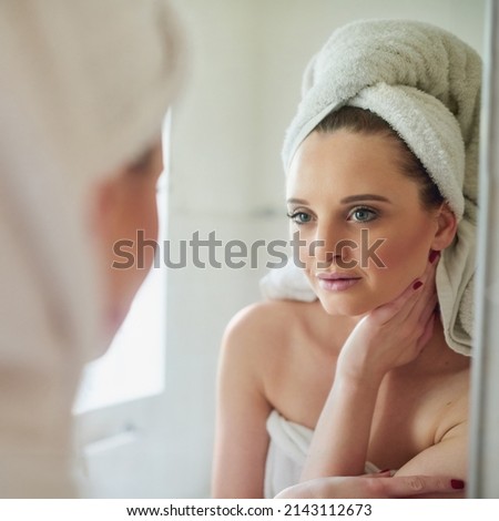 Her new beauty regime is really making her skin glow. Shot of an attractive young woman looking at herself in the bathroom mirror. Royalty-Free Stock Photo #2143112673
