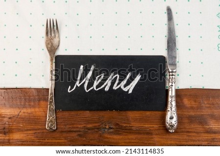 Menu written with chalk on aged blackboard with kitchen utinensil on wooden table. Top view