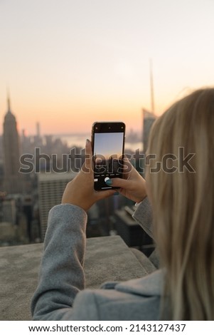 Girl with cell phone take a photo at sunset in New York City