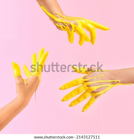 Creative concept of a raised hands dipped in yellow paint in the air. Pastel pink background. Royalty-Free Stock Photo #2143127511