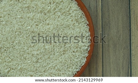 white rice (beras) on a wooden plate lacquered red brown with a wooden picture background. Rice is the seed of the grass species Oryza sativa (Asian rice) or less commonly Oryza glaberrima.