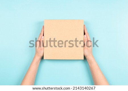 Female hands holding brown ecological package box made of natural corrugated cardboard. Mockup parcel box on light blue background. Top view. Packaging, shopping, delivery concept Royalty-Free Stock Photo #2143140267