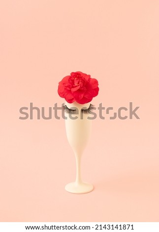 Creative composition made of glass with red flower and eyelashes on pastel pink background. Minimal summer or spring party concept.