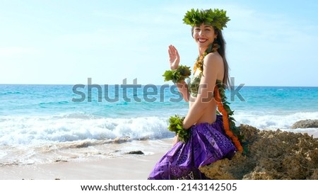 Happy and calm woman poses on the beach wearing the typical hula dance costume. The girl says hello to the clients. Lady receiving customers in a tropical place. Miss with a bikini waves the hand.