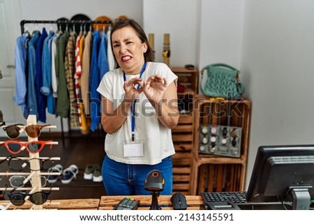 Beautiful middle age hispanic woman working as manager at retail boutique disgusted expression, displeased and fearful doing disgust face because aversion reaction. with hands raised 