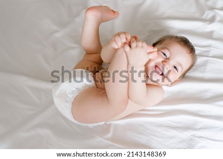 happy joyful baby in diapers lying on white bed Royalty-Free Stock Photo #2143148369