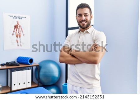 Young hispanic man wearing physiotherapist uniform standing with arms crossed gesture at clinic Royalty-Free Stock Photo #2143152351